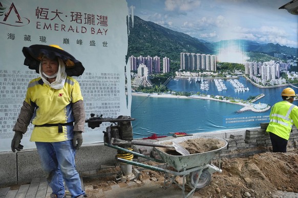 A worker walks past an advertisement photo of a property project of China Evergrande Group outside its headquarters in Hong Kong Monday, Oct. 4, 2021. Shares in troubled real estate developer China Ev ...