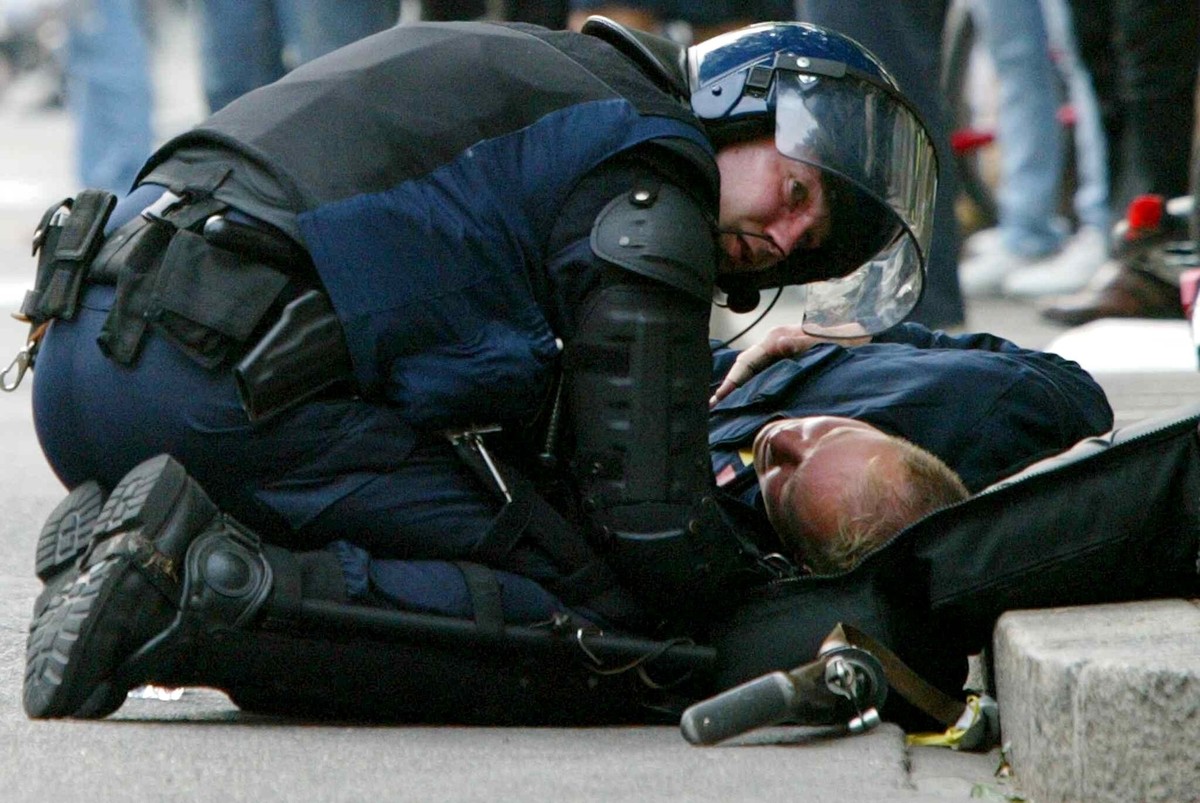 An injured riot police officer is helped by a colleague, during clashes with anti-globalisation protesters in Geneva, Switzerland, Tuesday, June 3, 2003. After the end of the G8 summit in Evian clashe ...