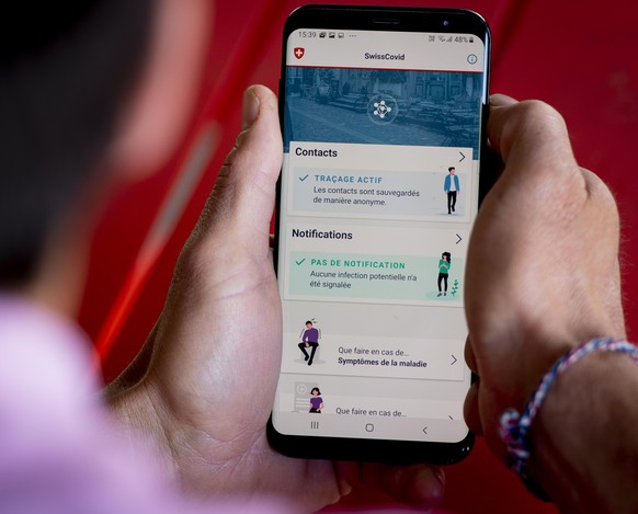 epa08443428 A man looking at a smartphone with the tracing app SwissCovid, using Decentralized Privacy-Preserving Proximity Tracing (DP-3T), during the state of emergency of the coronavirus disease (C ...