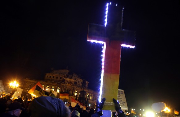 epa04538277 A supporter of the movement &#039;Pegida&#039; (Patriotic Europeans Against the Islamization of the Occident) holds an illuminated cross in the German national colors during a rally agains ...
