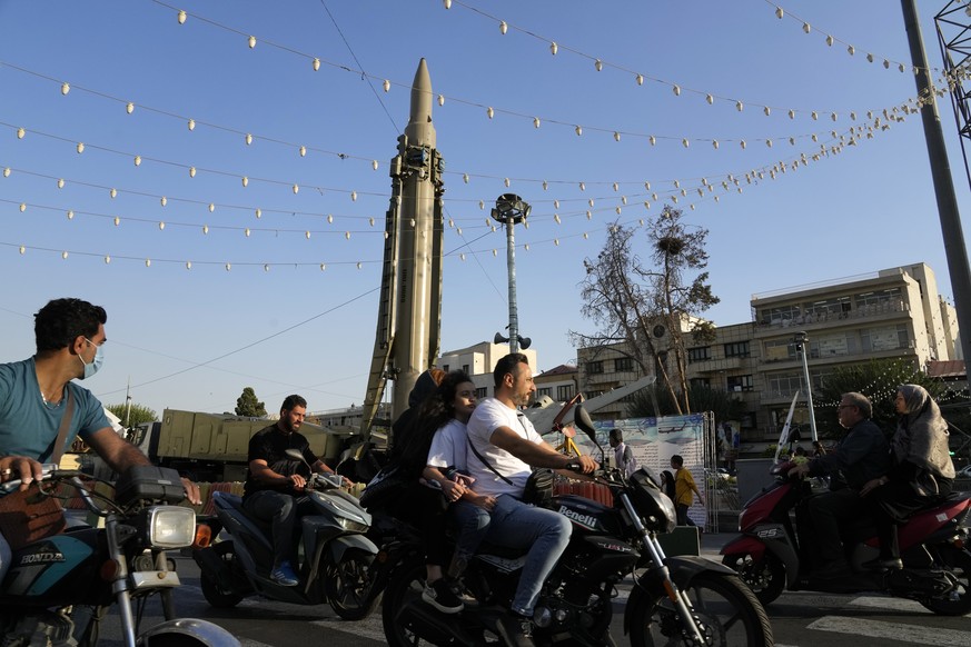 People ride their motorcycles in front of a Qiam missile displayed in an exhibition by Iran&#039;s army and paramilitary Revolutionary Guard celebrating &quot;Sacred Defense Week&quot; commemorating t ...