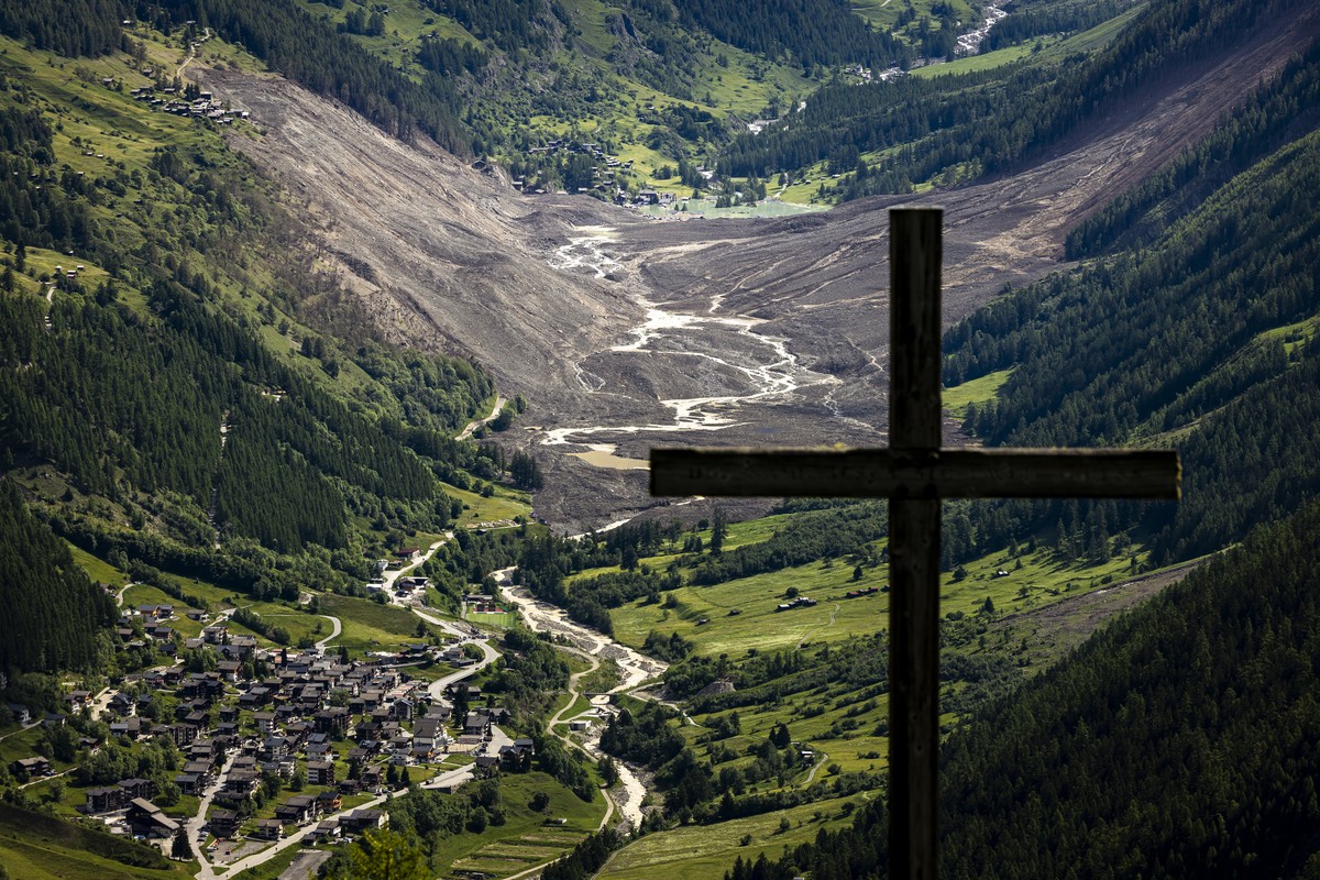 A wooden christian cross is silhouetted against the massive avalanche, triggered by the collapse of the Birch Glacier, swept down to the valley floor and demolishing the village of Blatten, rear, besi ...