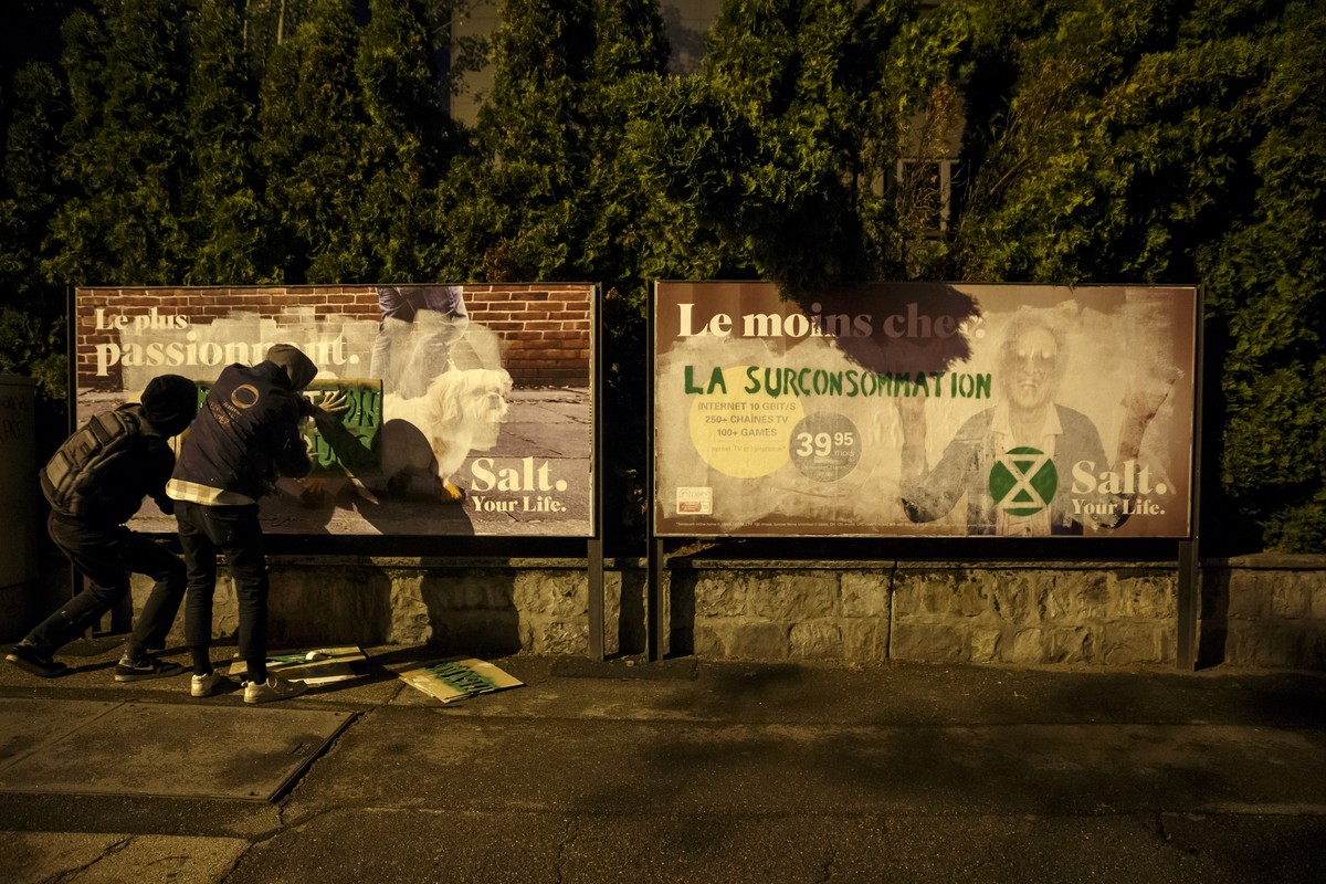 Des personnes ecrivent des messages "Pollution en Cours" "La surconsommation" sur des affiches publicitaires de Salt. pour protester contre le rechauffement climatique, lors d' ...