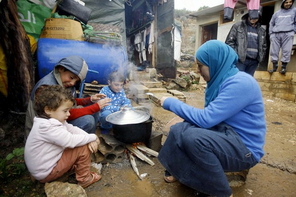 FILE - In this Wednesday December 11, 2013 file photo, a Syrian refugee woman with her children prepares food near her tent as a heavy snowstorm batters the region, in a camp for Syrians who fled thei ...