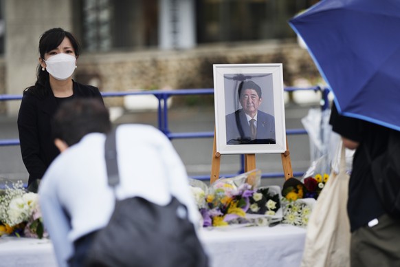 One of the staff members stands next to a picture of former Japanese Prime Minister Shinzo Abe as they receive bouquets of flowers from people visiting the memorial area set up at the ruling Liberal D ...