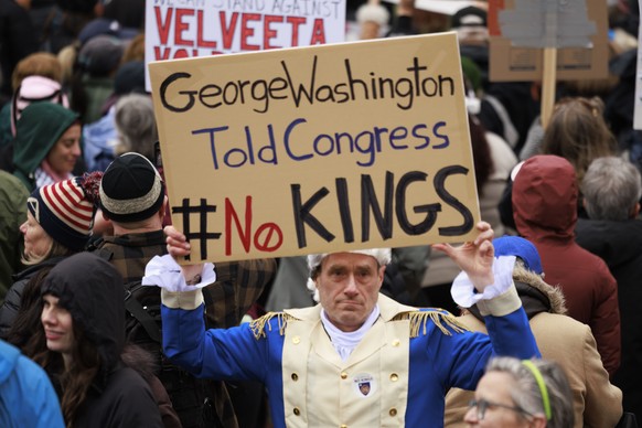 epa12012237 A man dressed as President George Washington carries a sign that reads 'George Washington Told Congress No Kings,' as he and thousands of people gather on Boston City Hall Plaza ...