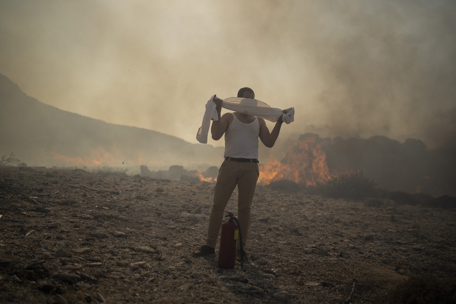 FILE - A man wraps his shirt over his face as he tries to extinguish a fire, near the seaside resort of Lindos, on the Aegean Sea island of Rhodes, southeastern Greece, on July 24, 2023. Europe is fac ...