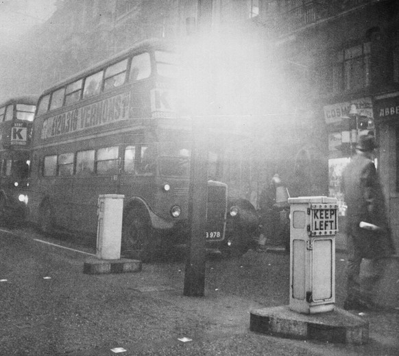 Two of London&#039;s double decker buses move slowly through fog shrouded streets, Dec. 5, 1962, as thick smog gripped the city for the second day. One bus has its headlights on as sunlight fails to f ...