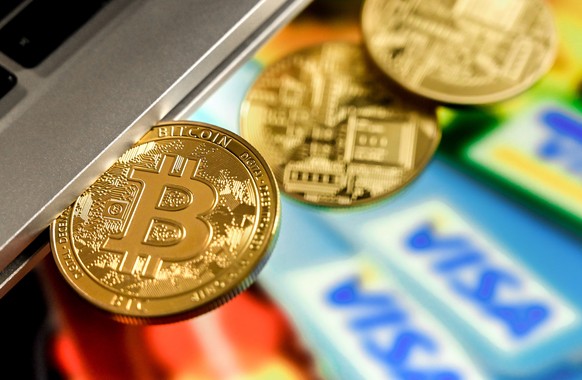 epa09018335 A bitcoin in a slot-in drive reflects in front of a monitor showing credit cards, in Duesseldorf, Germany, 17 February 2021. For the first time, the cryptocurrency Bitcoin has exceeded the ...