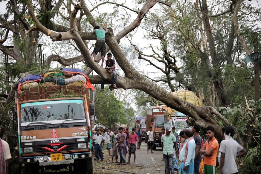 epa08435311 Commuters wait as locals try to remove an uprooted tree from the main road after Cyclone Amphan made landfall, in Bokkhali village near the Bay of Bengal, India, 21 May 2020. The Odisha go ...