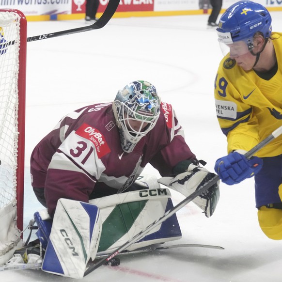 Goalie Arturs Silovs of Latvia, center, fights for a puck with Fabian Zetterlund of Sweden during the quarter final match between Latvia and Sweden at the ice hockey world championship in Riga, Latvia ...