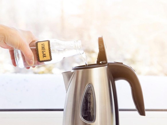 Woman pouring natural destilled acid white vinegar in electric kettle to remove boil away the limescale. Descaling a kettle, remove scale concept.

mit essig den wasserkocher reinigen