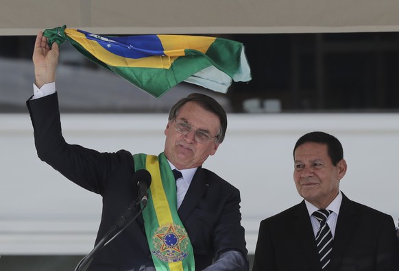 Brazil&#039;s President Jair Bolsonaro, flanked by his Vice President Hamilton Mourao, waves the national flag from the Planalto Presidential palace, in Brasilia, Brazil, Tuesday, Jan. 1, 2019. (AP Ph ...