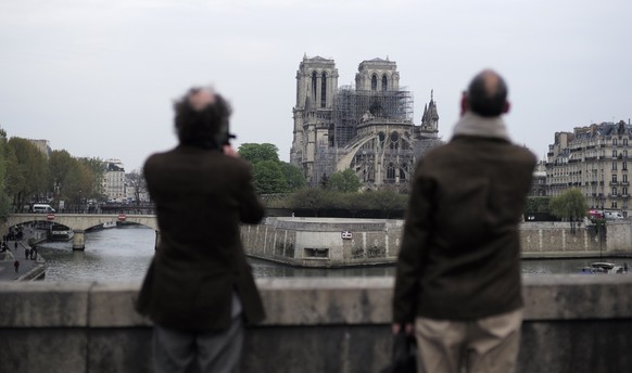 People stop to see and photograph the Notre Dame cathedral after the fire in Paris, Tuesday, April 16, 2019. Experts are assessing the blackened shell of Paris' iconic Notre Dame cathedral to establish next steps to save what remains after a devastating fire destroyed much of the almost 900-year-old building. With the fire that broke out Monday evening and quickly consumed the cathedral now under control, attention is turning to ensuring the structural integrity of the remaining building. (AP Photo/Kamil Zihnioglu)