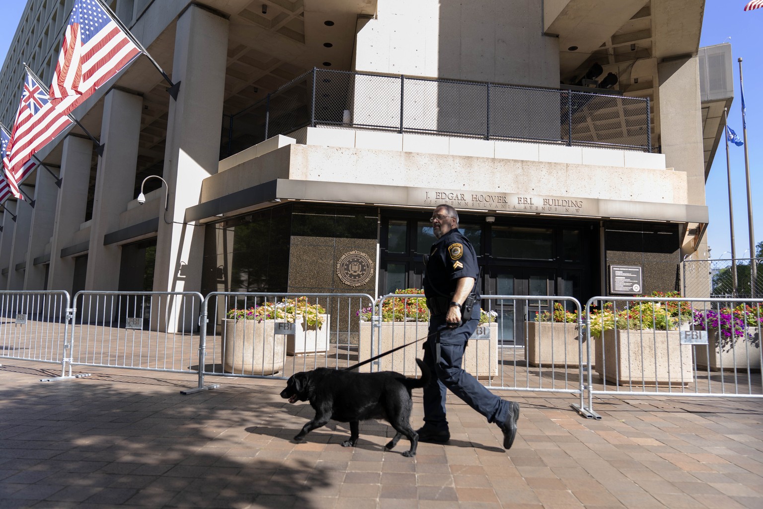 A Federal Bureau of Investigation police officer walks with his working dog outside Federal Bureau of Investigation building headquarters in Washington, Saturday, Aug. 13, 2022. (AP Photo/Jose Luis Ma ...