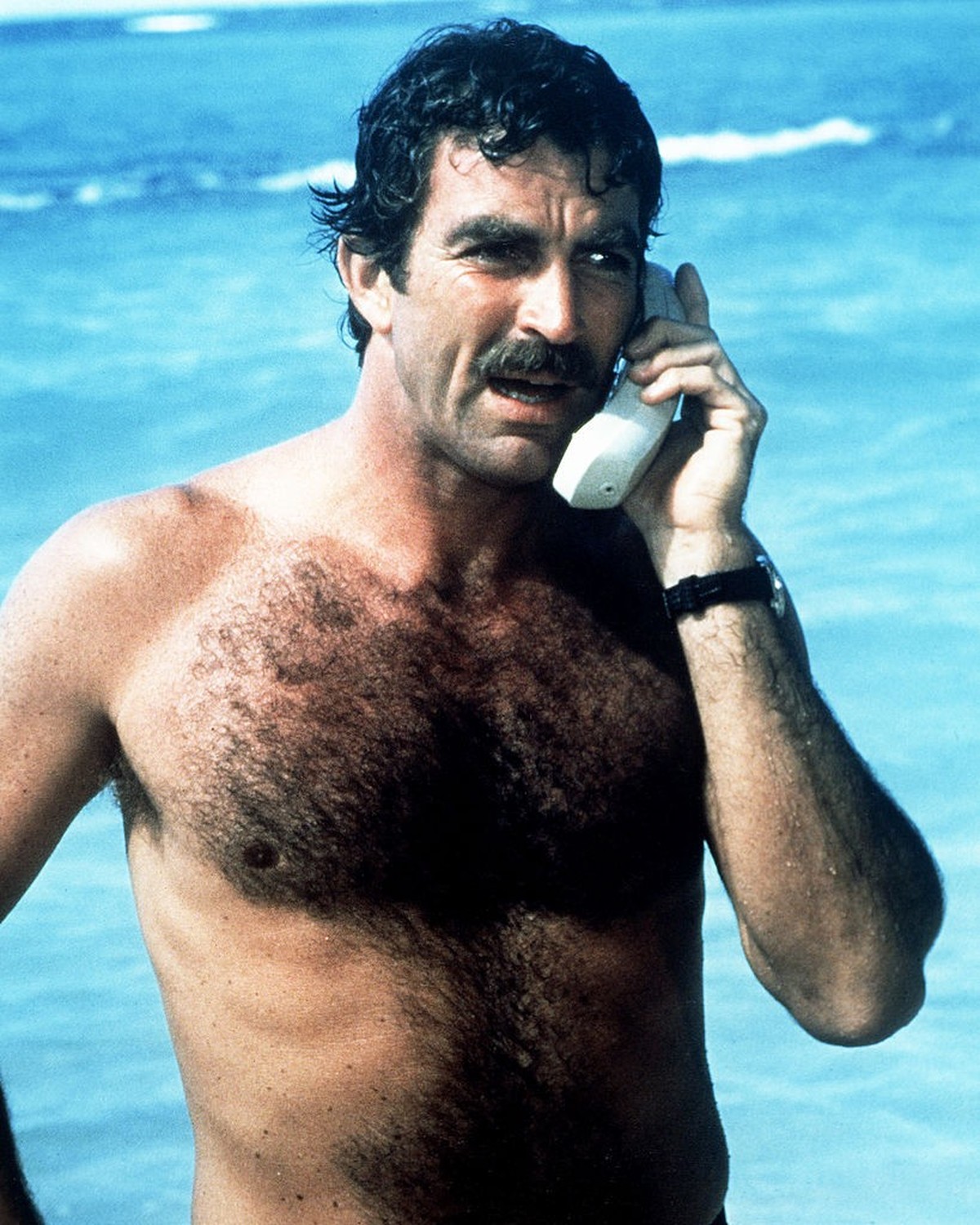 American actor Tom Selleck as Thomas Magnum, making a mobile phone call from the beach, in the American TV series 'Magnum PI', circa 1985. (Photo by Silver Screen Collection/Getty Images)