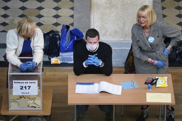 Volunteers wearing masks and gloves wait for voters in a polling station during local elections in Lyon, central France, Sunday, March 15, 2020. France is holding nationwide elections Sunday to choose ...