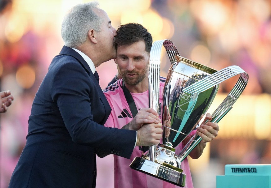 Inter Miami's Lionel Messi, centre, holds the trophy and receives a kiss on the head from managing owner Jorge Mas after defeating the Vancouver Whitecaps during the MLS Cup final soccer match, i ...