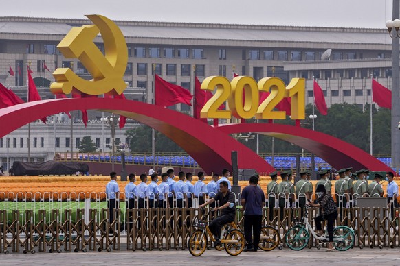 People cycle past Chinese paramilitary police standing in formation near seating and a platform with a Communist Party&#039;s logo setup on Tiananmen Square in Beijing, Monday, June 28, 2021. China is ...