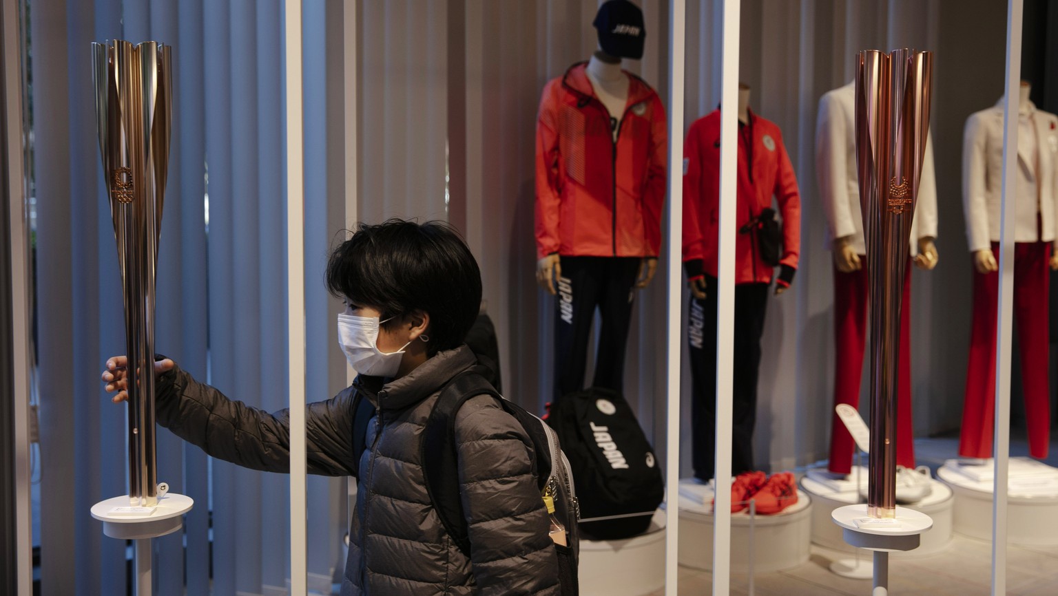 A boy with a mask poses with an Olympic torch of the Tokyo 2020 Olympics while visiting Tokyo Olympic Museum, Sunday, Feb. 23, 2020, in Tokyo. (AP Photo/Jae C. Hong)