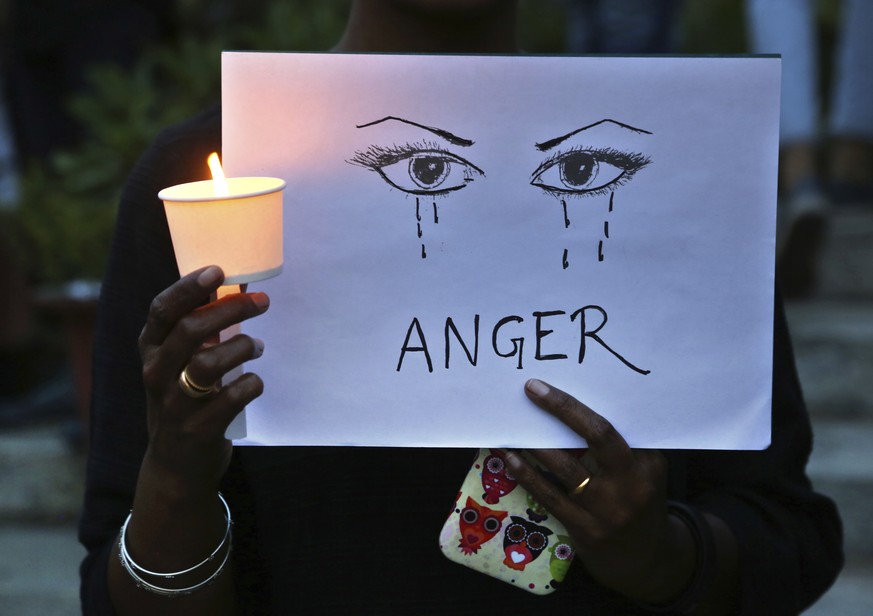 FILE - In this Monday, April 16, 2018 file photo, a woman holds a candle and placard seeking an end to sexual violence against women, which has been on the rise in the country, during a protest in Ban ...