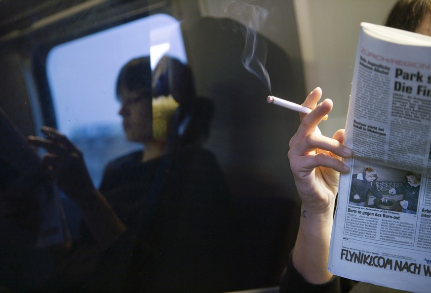 A woman smokes a cigarette and reads a newspaper in a smoking compartment of a train from Zurich to Winterthur, Switzerland, on November 9, 2005. (KEYSTONE/Martin Ruetschi)

Eine Frau raucht im Rauche ...