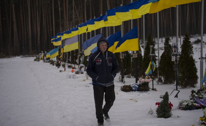 An undertaker walks by the Alley of Heroes at the Irpin Cemetery in Ukraine, Monday, Feb. 6, 2023. (AP Photo/Daniel Cole)