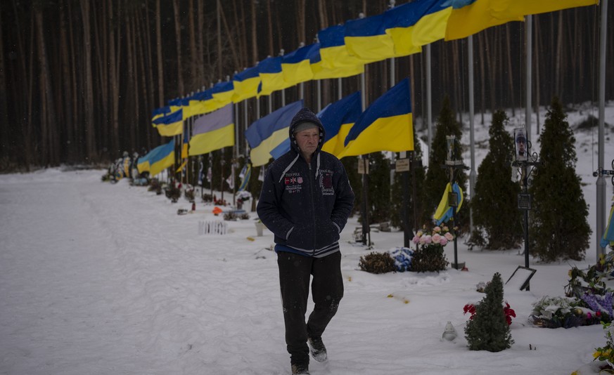 An undertaker walks along the Alley of Heroes at Irpin Cemetery in Ukraine, Monday, Feb. 6, 2023. (AP Photo/Daniel Cole)