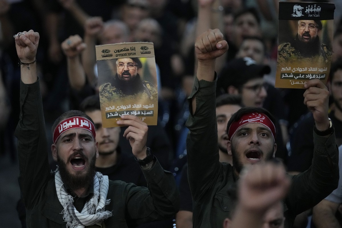 FILE -Hezbollah supporters shout slogans and hold up portraits that show the top commander Fouad Shukur, who was killed by an Israeli airstrike on Tuesday, July 30, during his funeral procession in a  ...