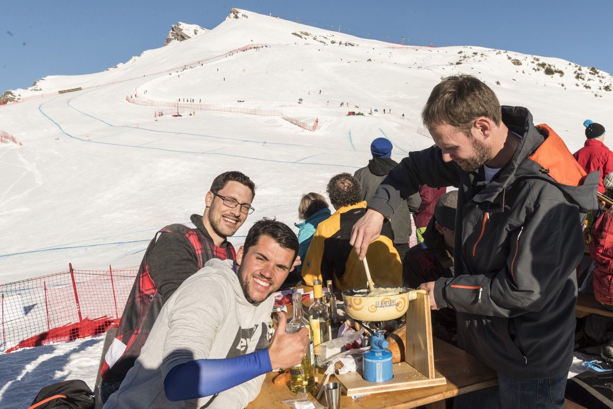 Spectators enjoy a cheese fondue, with the track and the Lauberhorn in the background, as a ski racer approaches the curve above the Hundschopf during the men's downhill race at the Alpine Skiing ...
