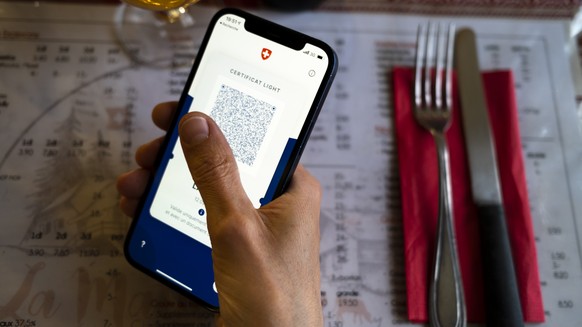 Une personne tient dans sa main un smartphone avec l&#039;application Certifact Covid suisse et un certificat light dans un restaurant ce vendredi 10 septembre 2021 a Rances dans le canton de Vaud. De ...