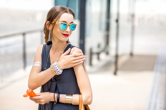 Young woman applying sunscreen lotion standing outdoors at the urban location during the sunny weather