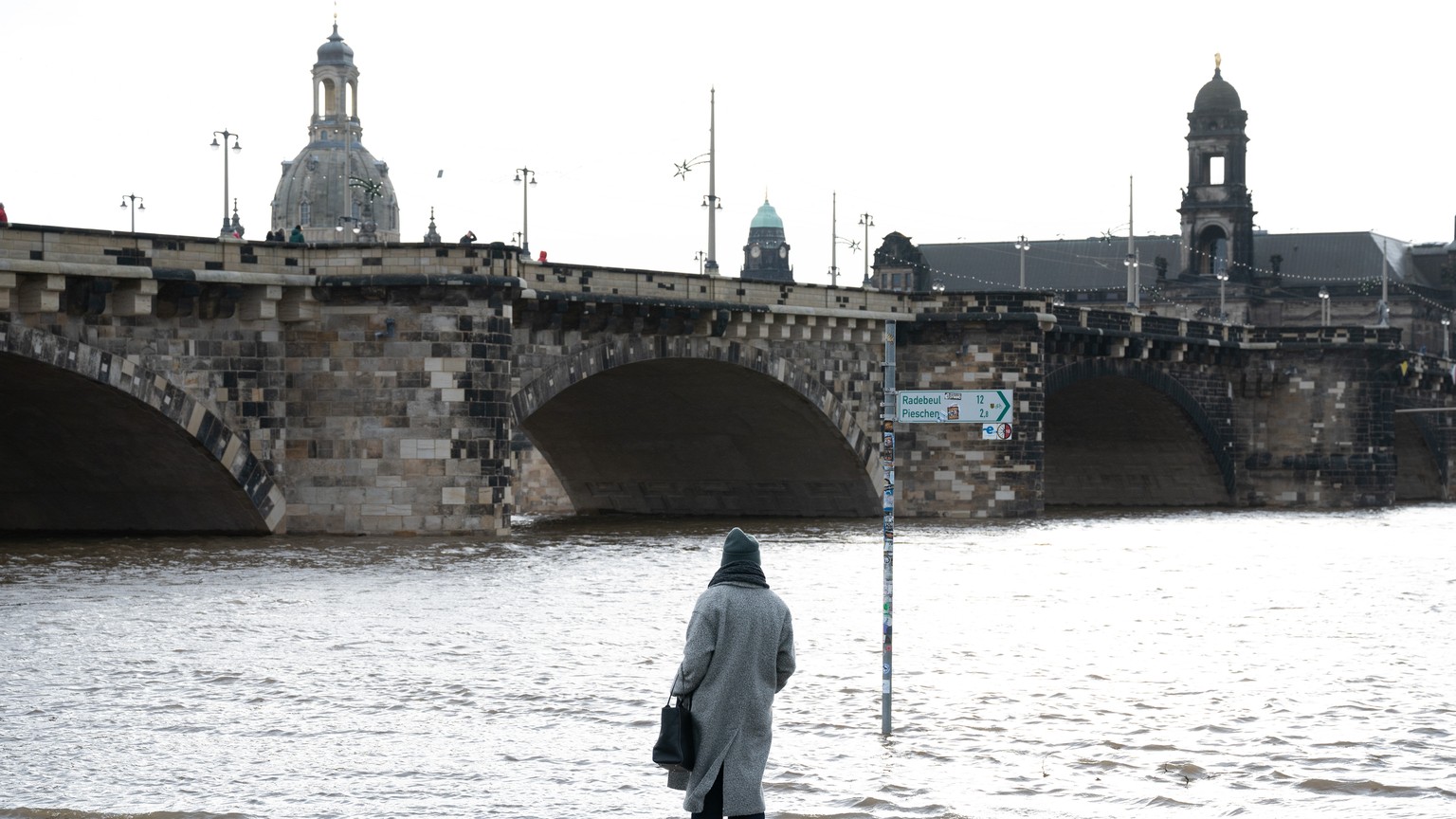 26.12.2023, Sachsen, Dresden: Eine Passantin steht an einem vom Hochwasser der Elbe