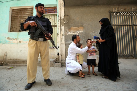 epa11599893 A police officer stands guard as a health worker administers polio vaccine drops to a child during a door-to-door vaccination campaign in Peshawar, Pakistan, 12 September 2024. A polio vac ...