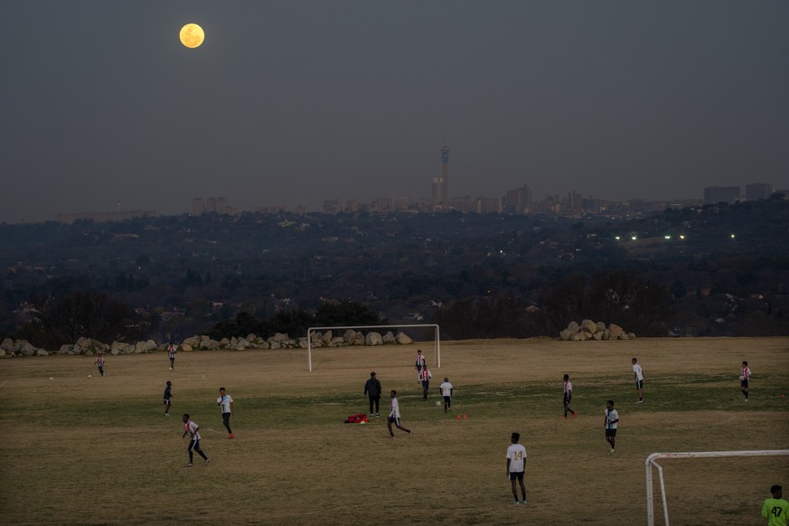With the city of Johannesburg and a rising supermoon in the background, young football players practice in Johannesburg, South Africa, Tuesday, Aug. 1, 2023. The moon appears slightly brighter and big ...