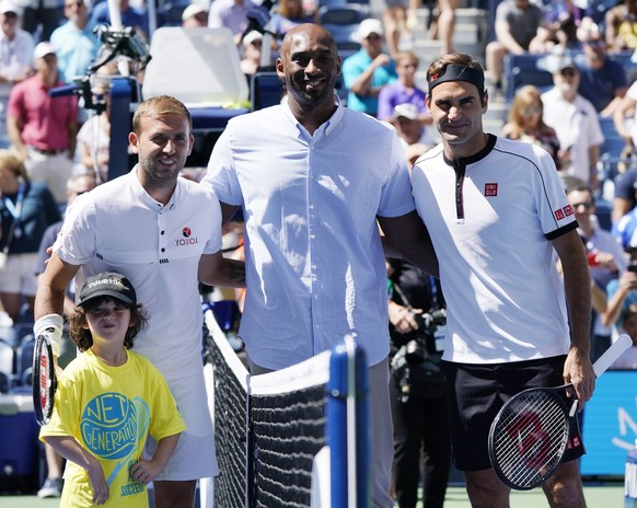 epa07804880 Former NBA player Kobe Bryant (C) before he tossed on the coin for the match between Roger Federer of Switzerland (R) and Daniel Evans of Great Britain (L) on the fifth day of the US Open  ...