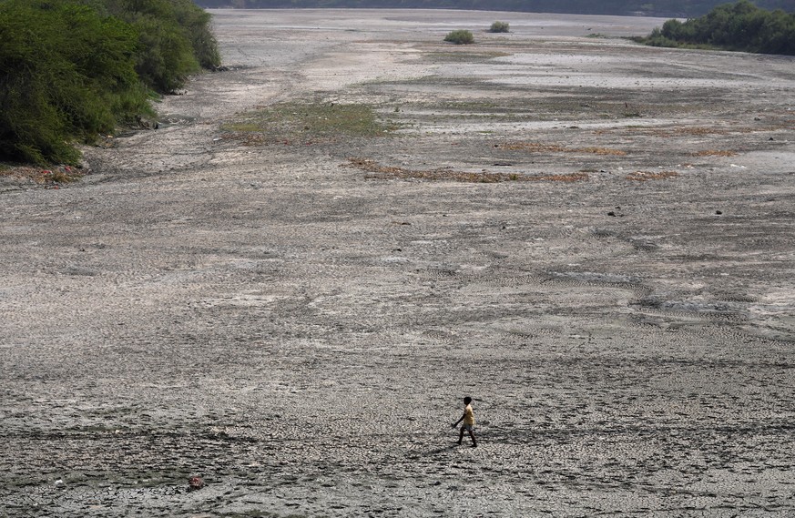 A man walks across an almost dried up bed of river Yamuna following hot weather in New Delhi, India, Monday, May 2, 2022. An unusually early and brutal heat wave is scorching parts of India, where acu ...