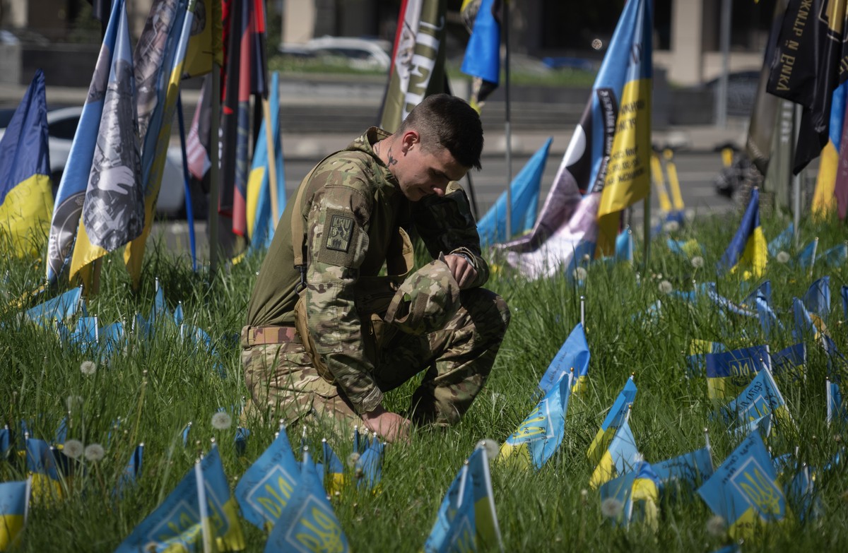 A soldier stands kneeling at the Independence square in Kyiv, Ukraine, Wednesday, May 1, 2024, surrounded by small national flags symbolising Ukrainian soldiers killed in the war with Russia. (AP Phot ...