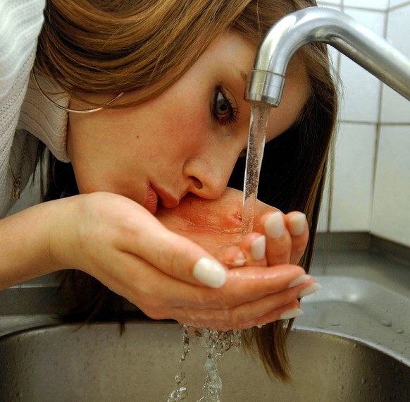 Eine junge Frau genehmigt sich einen Schluck Wasser aus dem Wasserhahn, aufgenommen in einer Kueche in Zuerich am 22. Maerz 2004. Schweizer Trinkwasser ist laut dem Zuercher Kantonslabor jedem Mineral ...