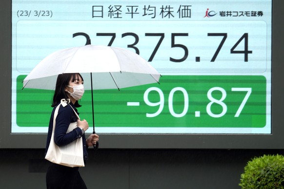 A person walks in front of an electronic stock board showing Japan's Nikkei 225 index at a securities firm in the rain on Thursday, March 23, 2023 in Tokyo.  Asian equities were mostly lower on Thursday…