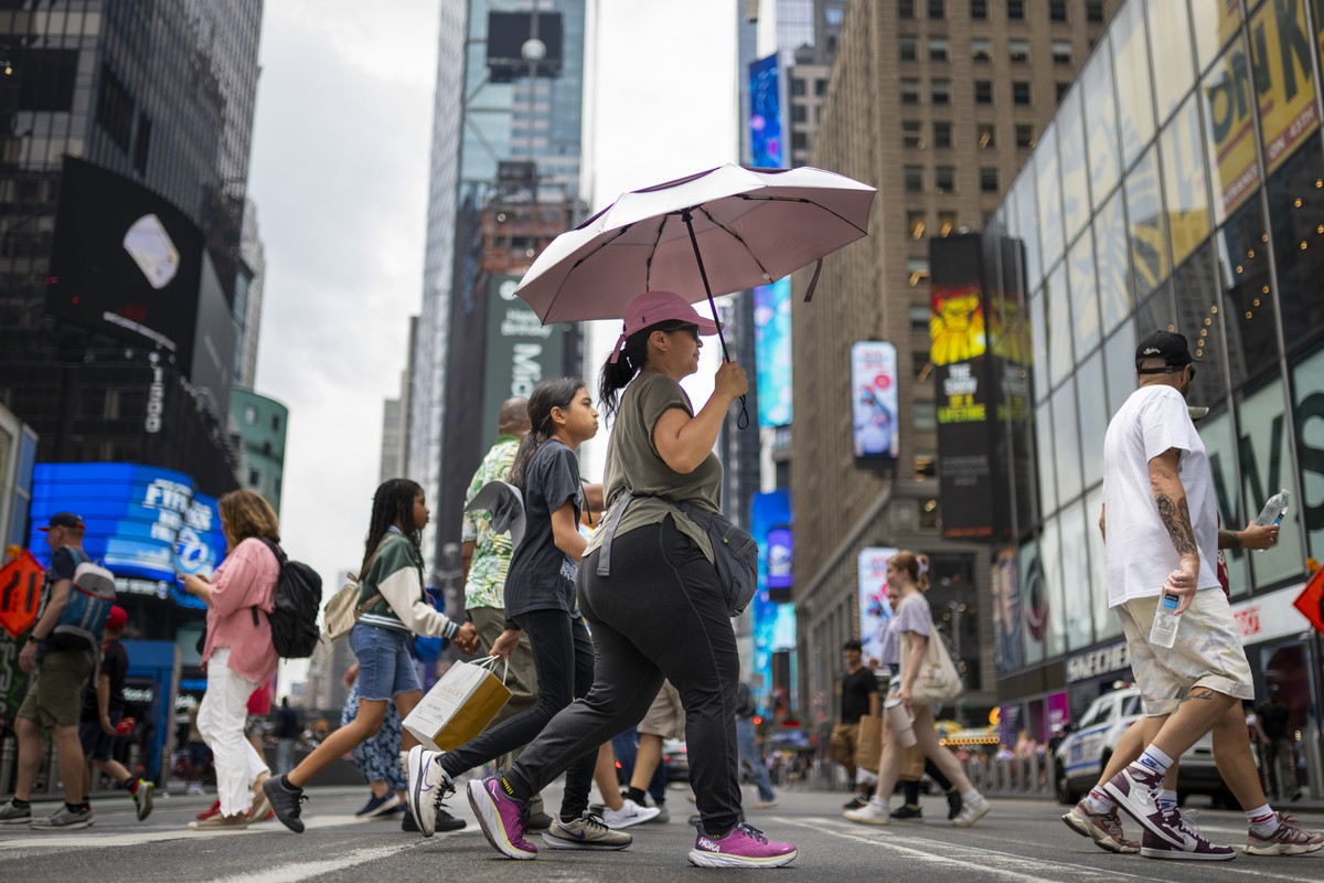 A pedestrian uses an umbrella to shield against the sun while passing through Times Square as temperatures rise, Thursday, July 27, 2023, in New York. Swaths of the United States are sweltering under  ...