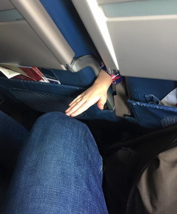 A child's hand reaches back between the seats on the plane