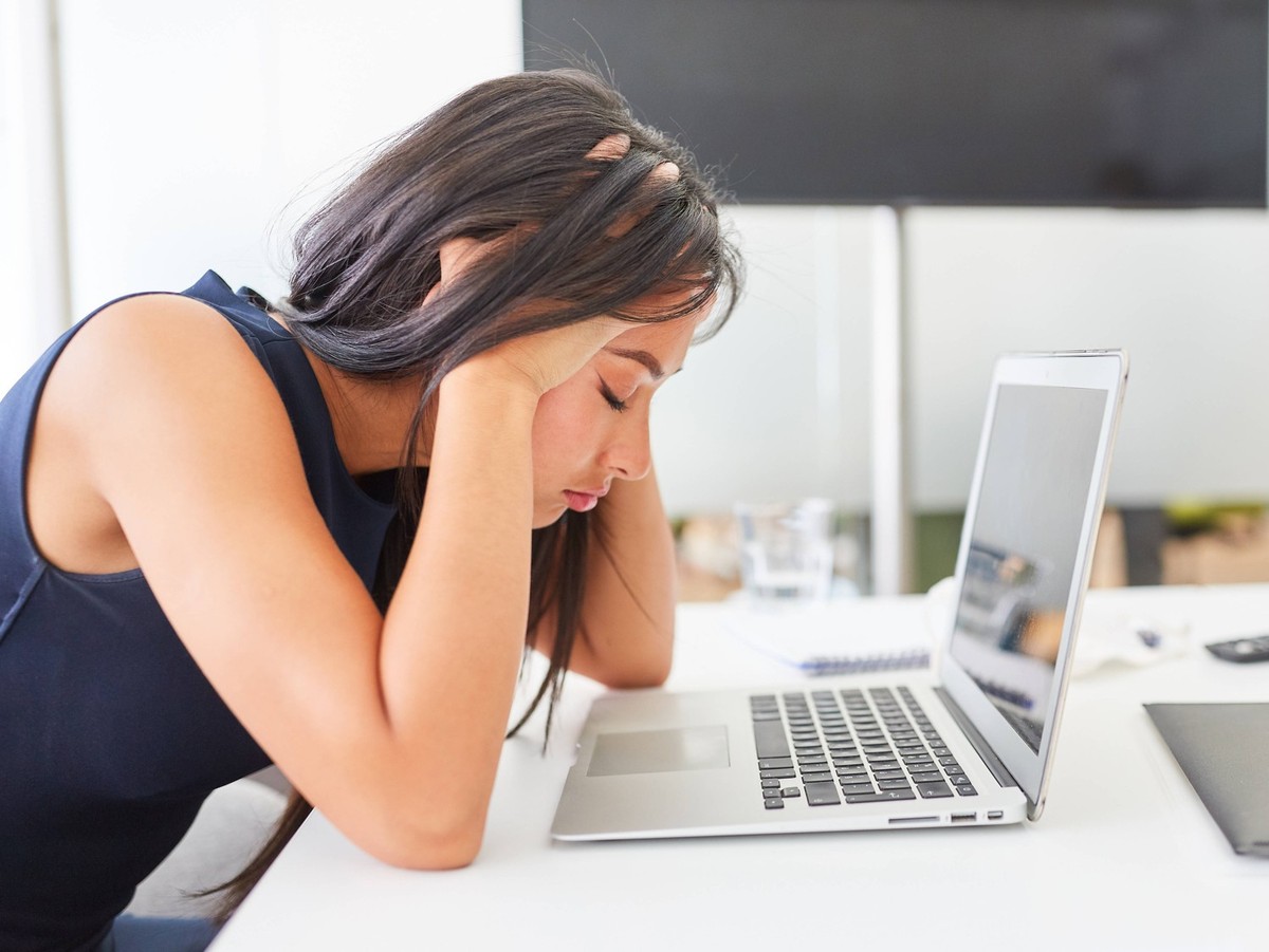 Junge Frau im Büro vor Laptop hält sich den Kopf (Symbolbild)