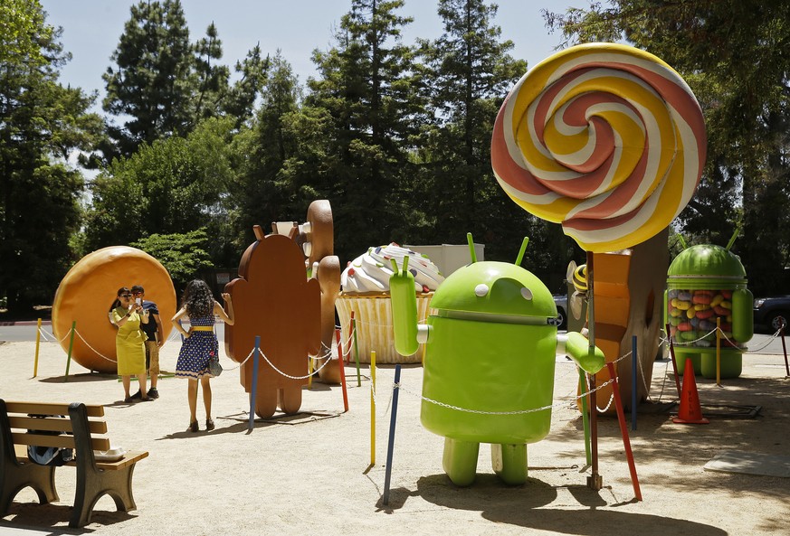 In this Wednesday, May 18, 2016, photo, people pose by Android lawn statues at Google&#039;s headquarters in Mountain View, Calif. The tall sculpture, at right, depicts the 2014 version of Android, kn ...