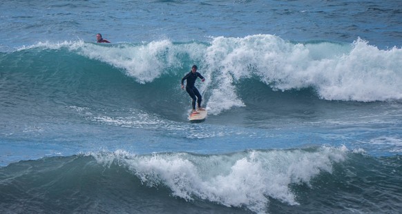 epa08962249 Two people enjoy surfing big waves in Andratx, Mallorca, 24 January 2021. The strong southwest wind keeps Mallorca on the orange alert, with warnings of waves of up to eight meters height. ...