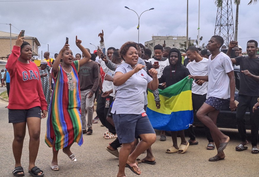 epa10828152 People display the Gabon national flag as they celebrate in the streets of Akanda, Gabon, 30 August 2023. Members of the Gabonese army on 30 August announced on national television that th ...