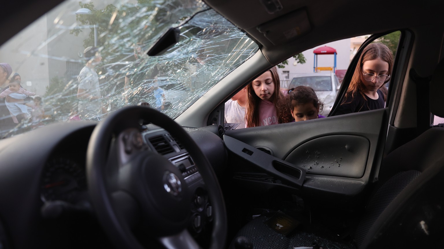 epa10604544 Children look at a damaged car at the site where a rocket landed outside a house in the southern city of Sderot, Israel, 02 May 2023. Militant groups in Gaza claimed responsibility for fir ...