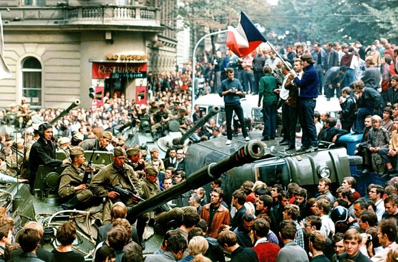 Prager Buerger mit tschechischer Flagge stehen auf einem umgestuerzten Wagen vor einem sowjetischen Panzer.