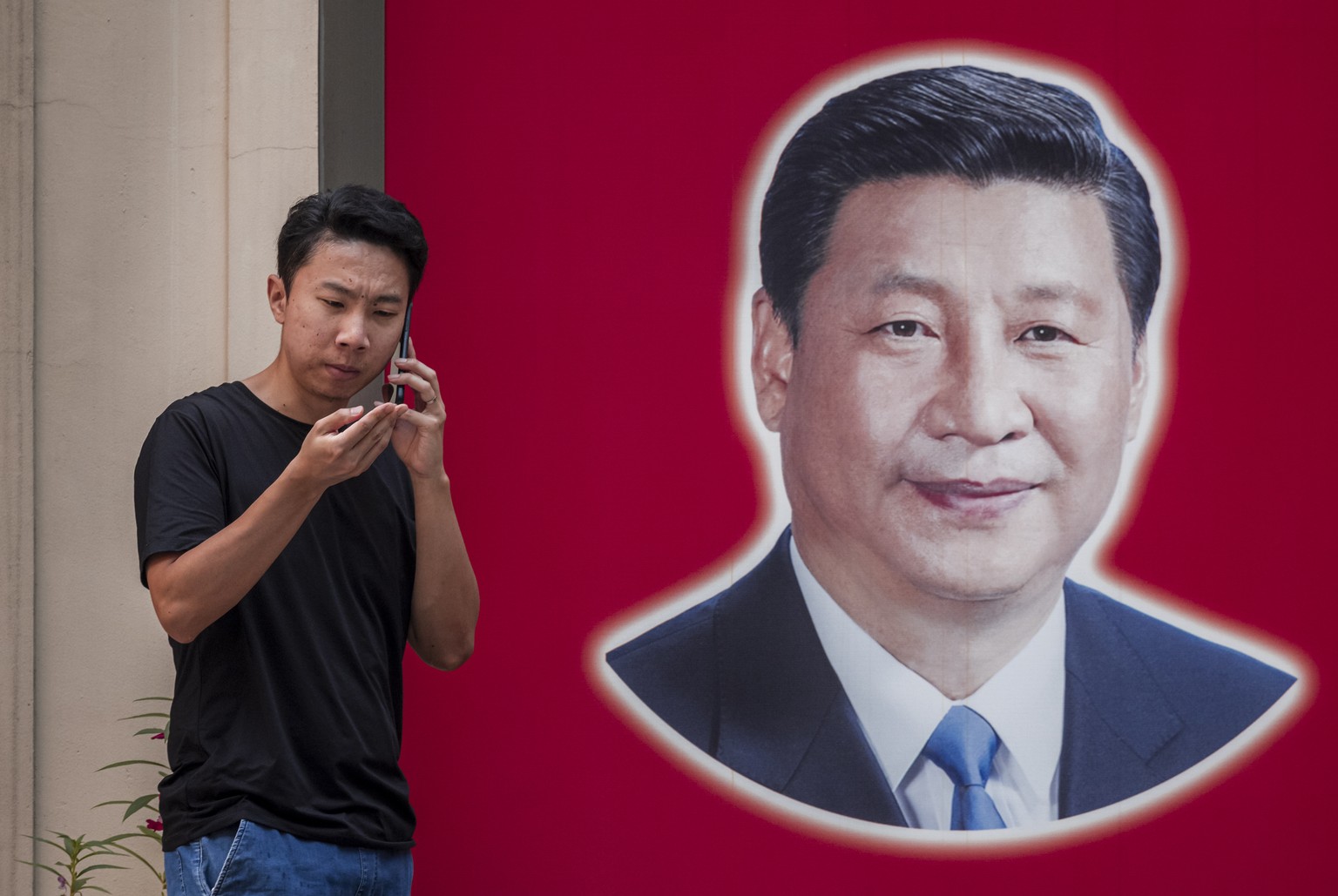 epa09430001 A man uses his phone next to the picture of the Chinese President Xi Jinping on the street in Shanghai, China, 26 August 2021. &#039;Xi Jinping Thought on Socialism with Chinese Characteri ...