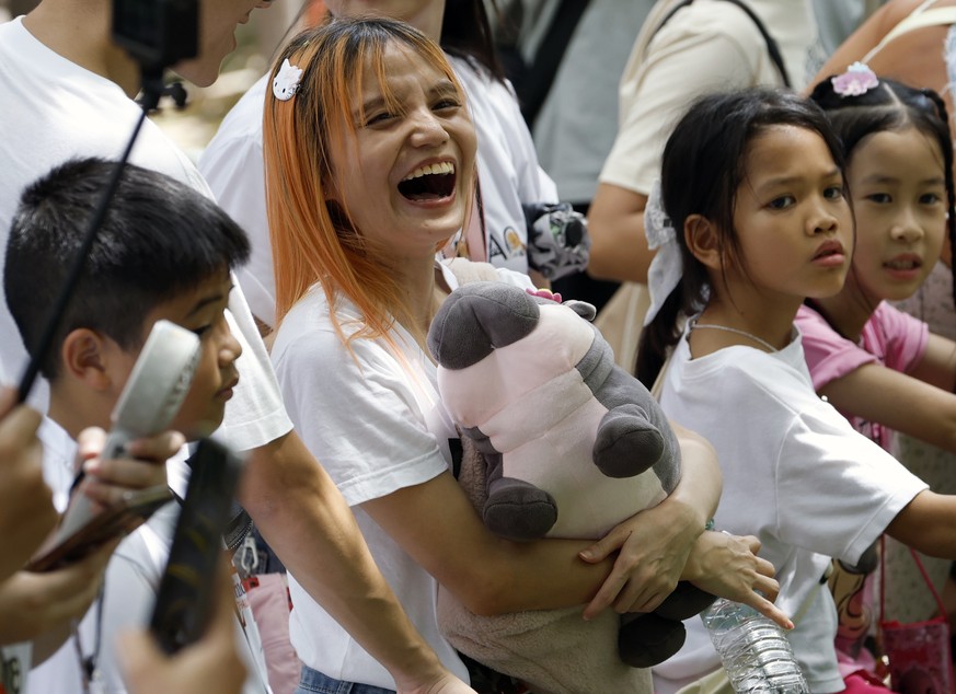 epa12228705 A visitor holding a Moo Deng doll laughs during the first birthday celebrations of the world?s most famous one-year-old female pygmy hippopotamus, Moo Deng, at Khao Kheow Open Zoo in Chonb ...